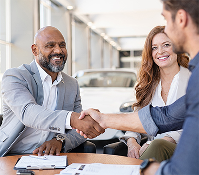 Dealership employee smiling shaking hands with satisfied customer.